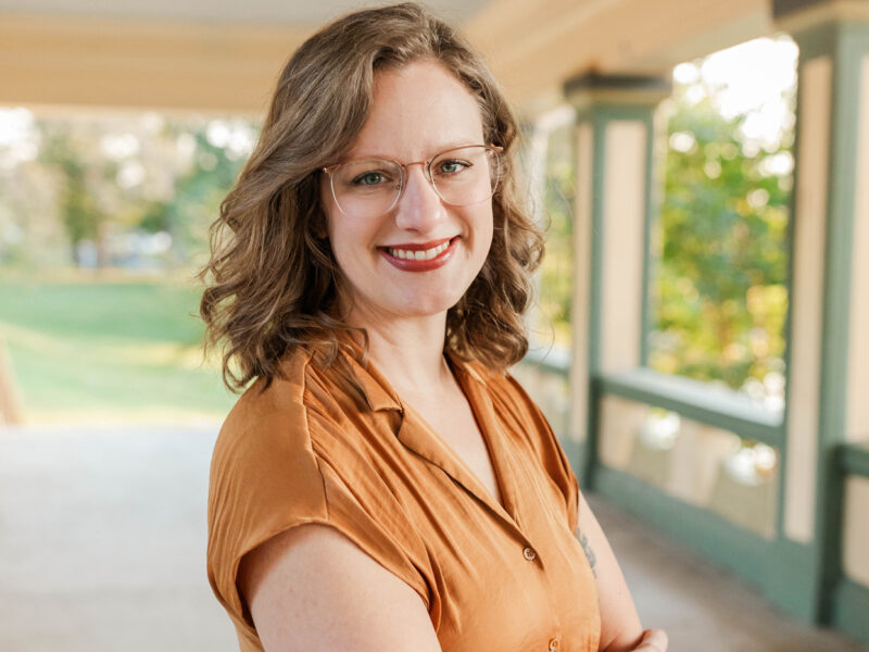 Woman arms folded, outside in the summer time wearing a yellow blouse.