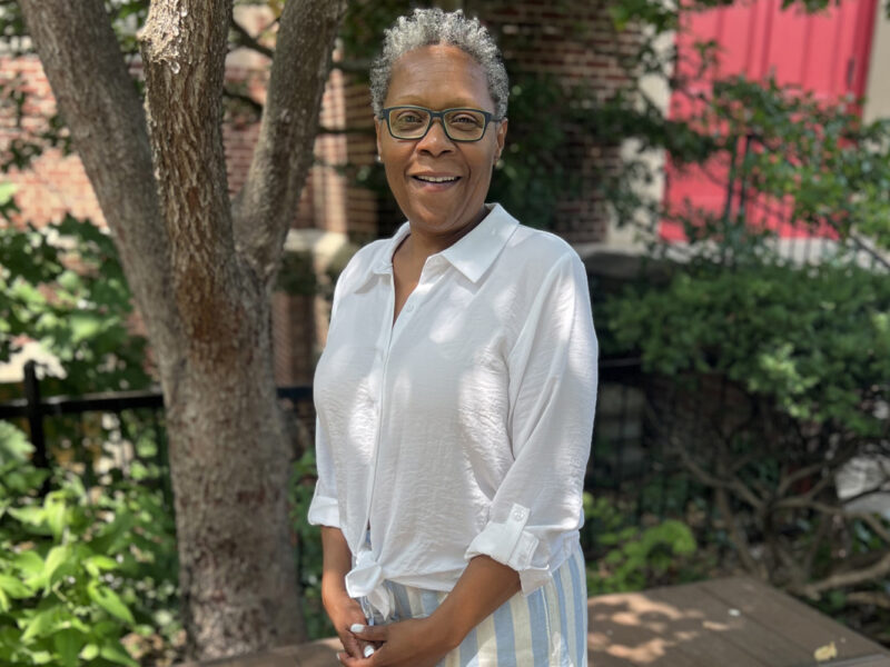 Woman outside of the red doors of the church wearing a white blouse, smiling