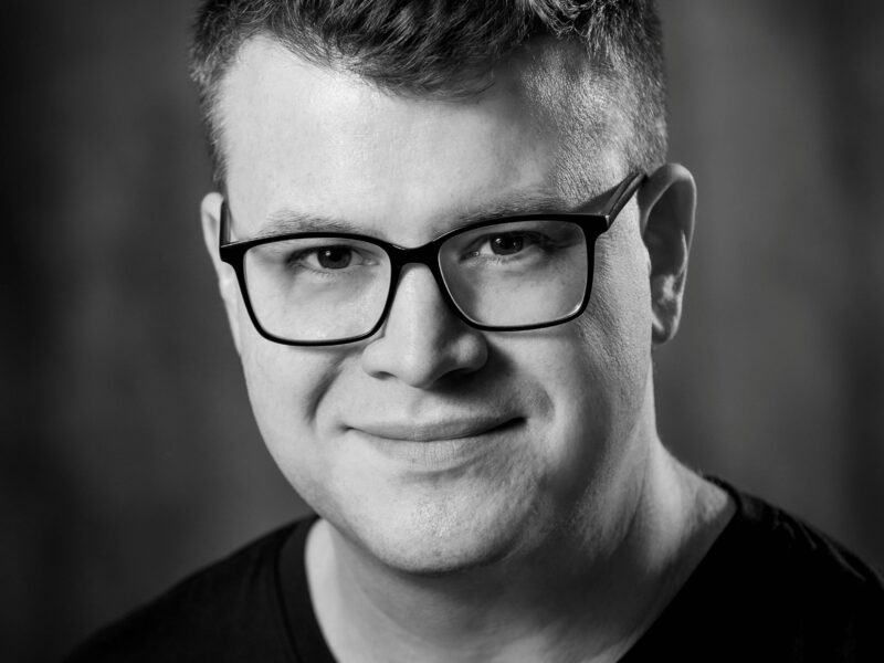 Black and white headshot of a man wearing glasses.